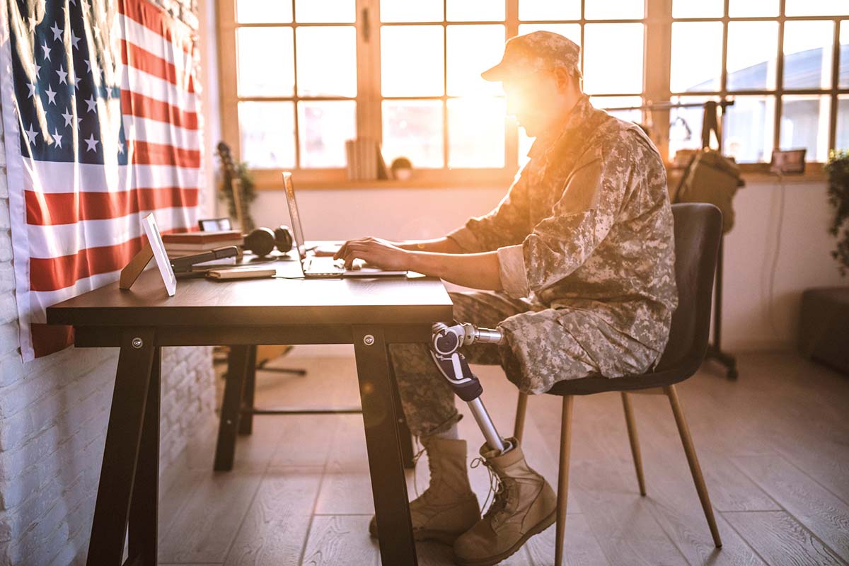 Veteran with amputated leg sits at a desk in from of the American flag